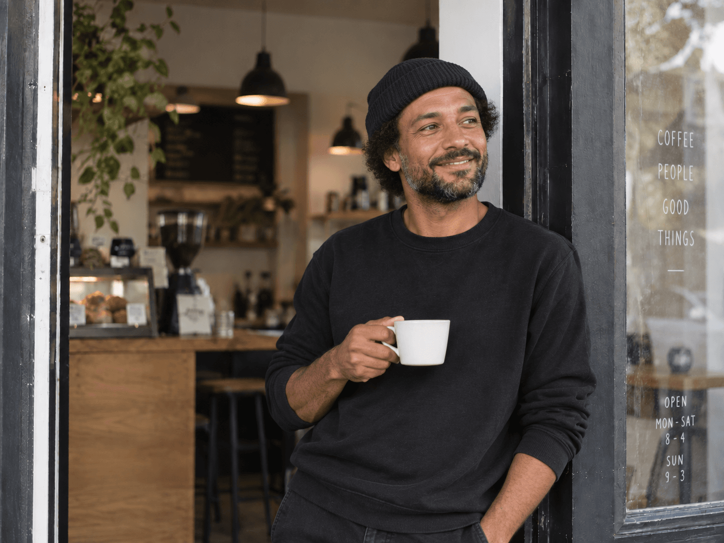 A café owner in his doorway with a cup of coffee.